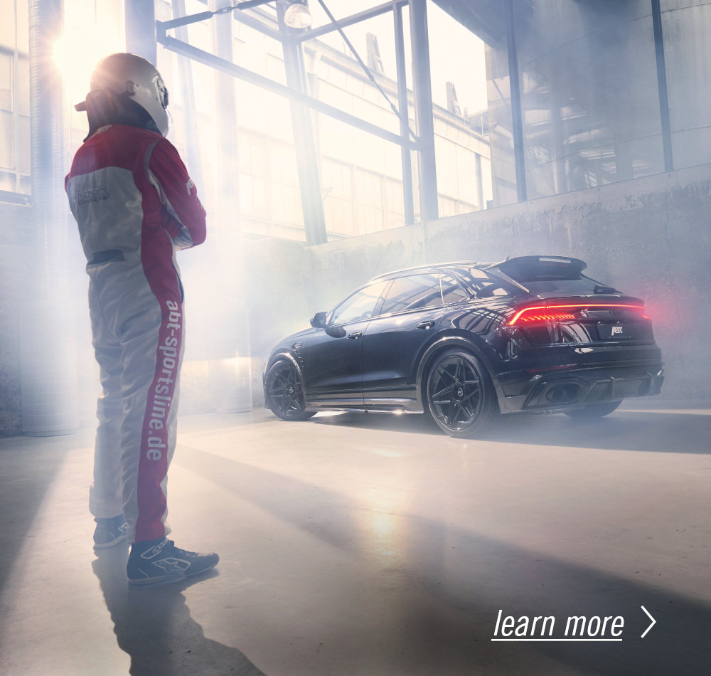 A racing driver looks at a black RSQ8 in a warehouse